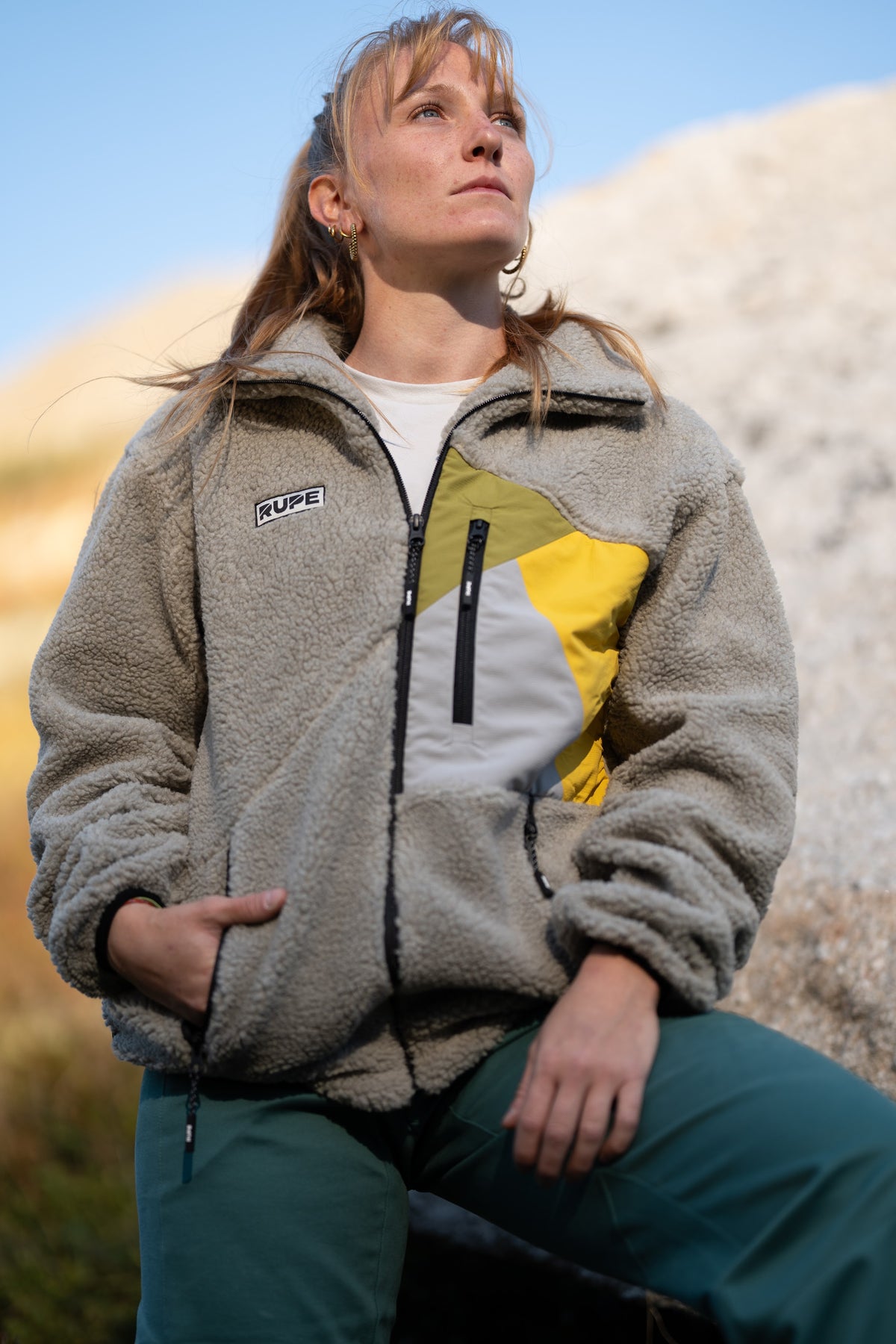 FW26-126 Yeti 2.0 Sunny + Ande Forest (donna seduta, guarda in alto, cielo blu)